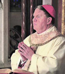 Cardinal Tobin standing a podium, with his fingertips together in prayer.
