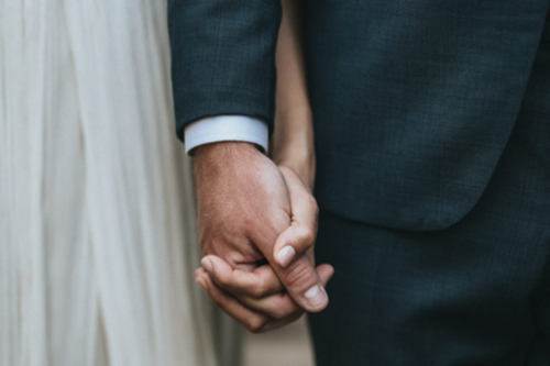 An image of a couple dressed in wedding clothing holding hands